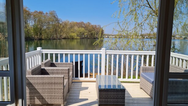 A deck with wicker furniture and a glass-top table overlooking a calm lake.