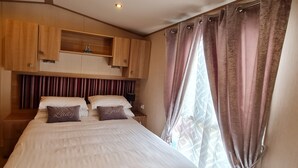 A bedroom with a large bed, wooden cabinets above, and a window with curtains.