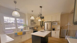 A modern kitchen with white cabinets, a central island, stainless steel appliances, and pendant lighting.