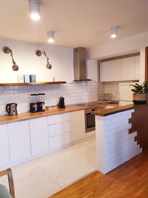 A modern kitchen with white cabinets, a wooden countertop, and a built-in oven. There are two coffee makers and a kettle on the counter. - Duplex 150m2 - Central Station best location in town (Skopje)