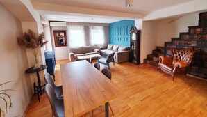 A spacious living area with a wooden dining table, sofas, and a staircase with bookshelves. - Duplex 150m2 - Central Station best location in town (Skopje)