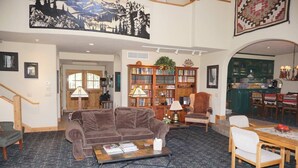 A cozy living room with a brown sofa, a coffee table, and a bookshelf. There is a staircase on the left and a dining area with a table and chairs on the right. - Ski-in/Ski-out Access Quiet location at end of Cul-de-Sac (203048-9004) (Snowmass Village)