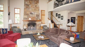 A spacious living room with a stone fireplace, comfortable seating, and a staircase leading to an upper level. - Ski-in/Ski-out Access Quiet location at end of Cul-de-Sac (203048-9004) (Snowmass Village)