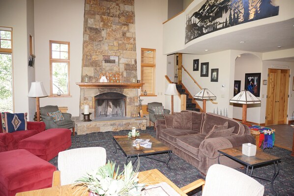 Un salón espacioso con chimenea de piedra, asientos cómodos y una escalera que lleva a un nivel superior.