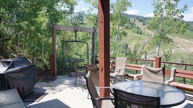 A wooden deck with outdoor furniture, a covered grill, and a swing set overlooking a mountainous landscape. - Ski-in/Ski-out Access Quiet location at end of Cul-de-Sac (203048-9004) (Snowmass Village)
