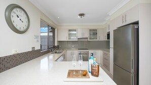 Una cocina moderna con un refrigerador de acero inoxidable, un reloj en la pared y una encimera con dos copas de vino y una botella.