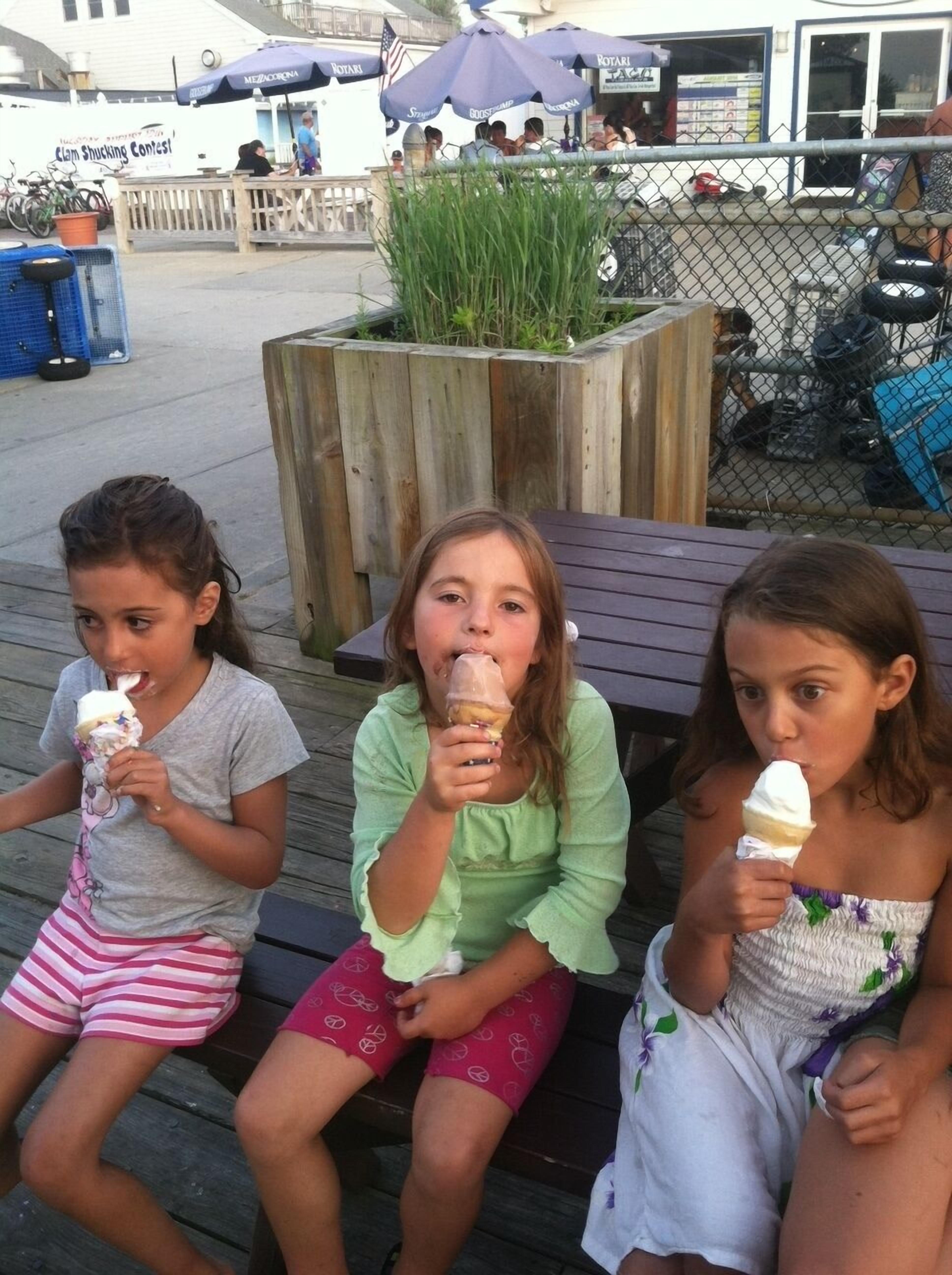 Three children sitting on a wooden bench eating ice cream cones.