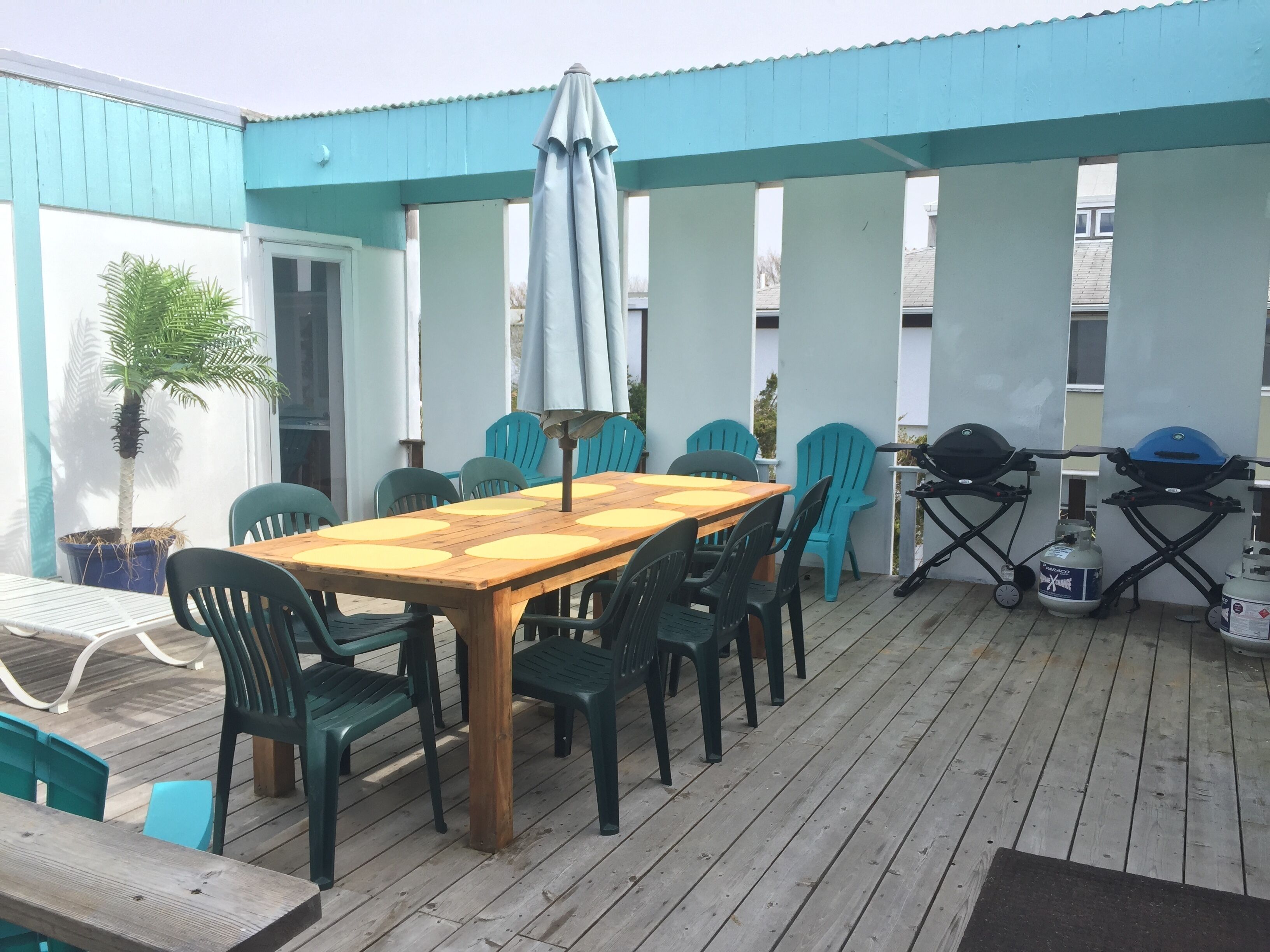 An outdoor patio with a wooden table and chairs, a grill, and a potted plant.