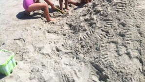 Drie kinderen spelen op een zandstrand, met de oceaan op de achtergrond.