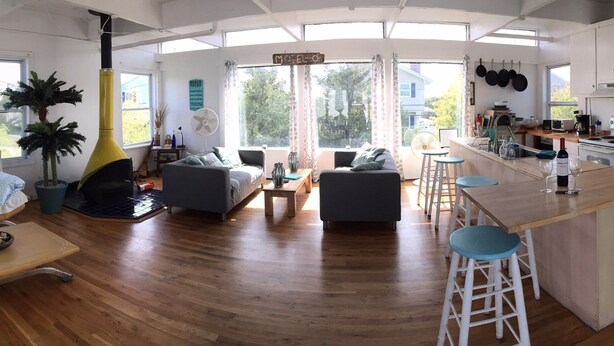 Een ruime woonkamer met een bank, een eettafel en een keuken met een koelkast en fornuis.