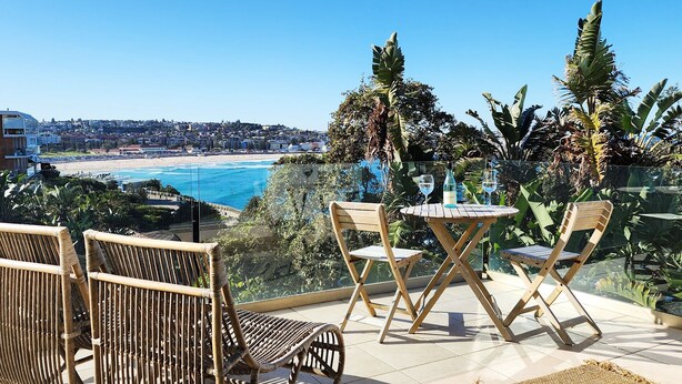 Een balkon met rieten stoelen en een tafeltje, met uitzicht op een strand en stadsbeeld.