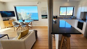 Een moderne keuken met een groot eiland, een eethoek met uitzicht en een woonruimte met een bank en televisie.