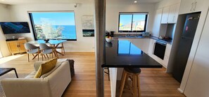 A modern kitchen with a large island, a dining area with a view, and a living space with a sofa and TV.