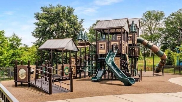 A playground with slides and climbing structures, surrounded by a fence and trees. - July Fun! Happy & Chill in West Nashville! (Nashville)