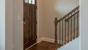 A hallway with wooden flooring, a wooden door, and a white staircase with a black railing. - July Fun! Happy & Chill in West Nashville! (Nashville)