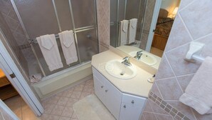 A bathroom with a glass-enclosed shower, two sinks, a large mirror, and a white tiled floor.
