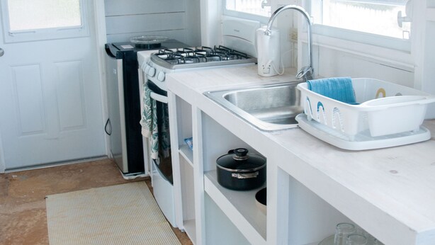 Een kleine keuken met witte keukenkastjes, een gasfornuis, een spoelbak en een raam voor natuurlijk licht.