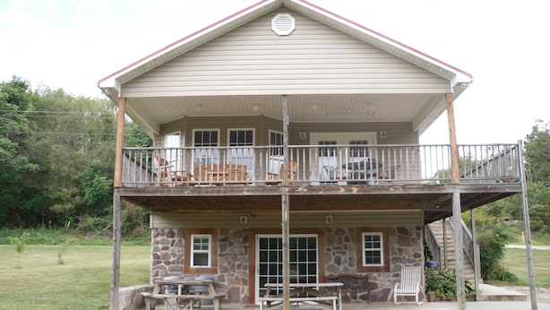 A two-story building with a balcony, stone foundation, and outdoor seating area. - Welcome to Tranquility (Ivanhoe)