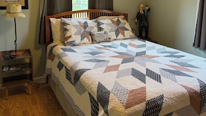 A bedroom with a wooden ceiling, a bed with a quilt, a nightstand, a lamp, a window with curtains, and a wall-mounted picture. - Welcome to Tranquility (Ivanhoe)