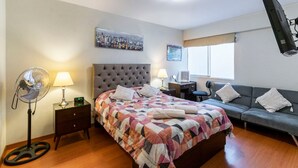 A bedroom with a bed, a nightstand, a fan, a sofa, and a window with curtains. - Modern And Safe Miraflores Apartment (Miraflores)