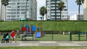 A playground with a fenced area, a stroller, and a person walking. - Modern And Safe Miraflores Apartment (Miraflores)