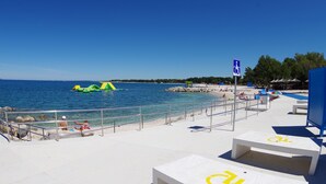 A beach area with a clear blue sky, a lifeguard tower, and a wheelchair-accessible sign. - Cozy apartment only 500m from the beach (Štinjan)