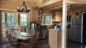 A wooden cabin kitchen with a dining area, wooden cabinets, a stainless steel refrigerator, and a hanging light fixture.