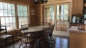 A wooden cabin interior with a dining table, chairs, and a kitchen area.