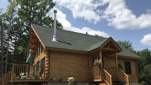 A log cabin with a porch, a chimney, and a deck.