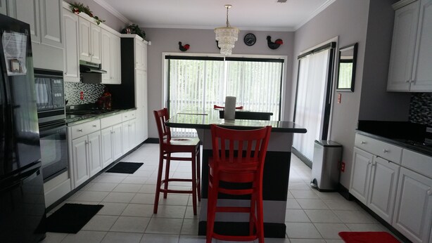 Una cocina con gabinetes blancos, encimera negra y una mesa de comedor con sillas rojas.