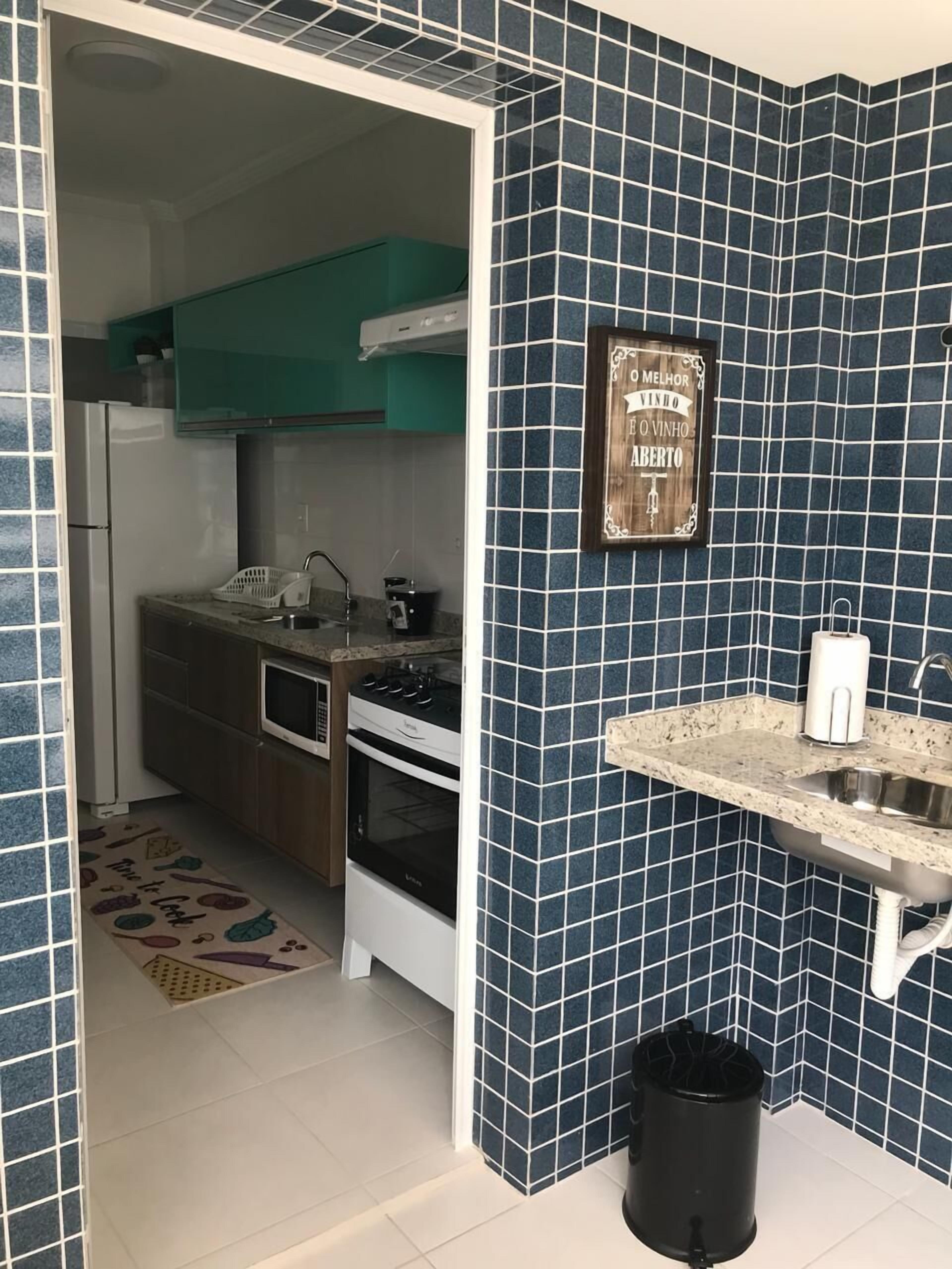 Una cuina compacta amb parets de rajola blava fosca, un armari de fusta, una placa de cocció i un rentapeus.