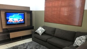 Ett vardagsrum med en platt-TV som är monterad på en möbel i trä, en mörkgrå soffa med mönstrade kuddar och en grå, lurvig matta.