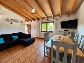Una sala de estar con sofá, mesa de comedor, sillas, televisor y ventana con vistas.