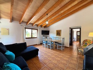 A living room with a sofa, dining table, chairs, a TV, and a kitchen area.