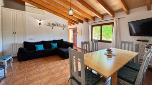 Une pièce chaleureuse avec un plafond en bois, un canapé agrémenté de coussins turquoise, une table à manger avec des chaises, un téléviseur et une fenêtre donnant sur un paysage verdoyant.