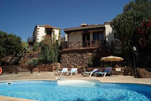 A pool area with lounge chairs and a stone wall. - Casa Rural El Olivar - La Almazara (Valle, El (Santa Lucia De Tirajana))