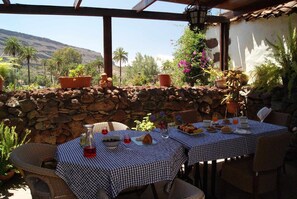 An outdoor dining area with stone walls, wicker chairs, and checkered tablecloths. - Casa Rural El Olivar - La Almazara (Valle, El (Santa Lucia De Tirajana))