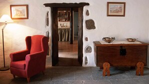 A room with a red armchair, a wooden table with a metal bowl, and a doorway leading to a kitchen area.