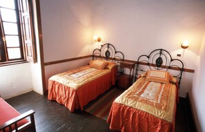 A room with two single beds, each with a wooden headboard and a red bedspread. There are two wall-mounted nightstands with lamps, and a window with a wooden frame on the left. - Casa Rural El Olivar - La Almazara (Valle, El (Santa Lucia De Tirajana))