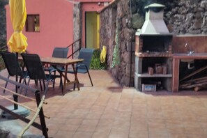 Une terrasse extérieure avec une table et des chaises, un barbecue et un mur en pierre.