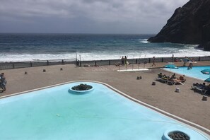 Ein Poolbereich mit Blick auf den Ozean, eine felsige Klippe und ein umzäunter Weg.