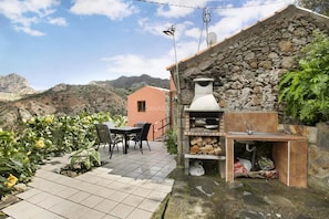 Une terrasse avec une table et des chaises, un mur en pierre, une cheminée et une vue sur la montagne.