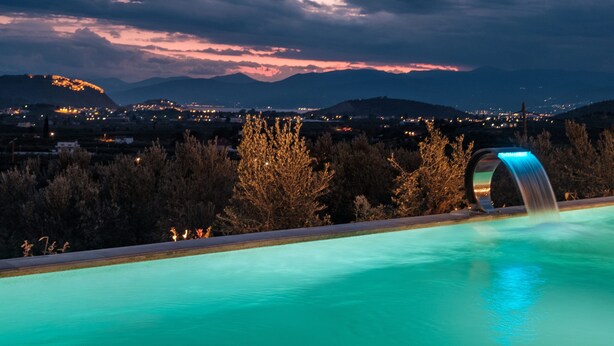 Une piscine agrémentée d’un élément décoratif aquatique, entourée d’arbres et avec un paysage montagneux en toile de fond.