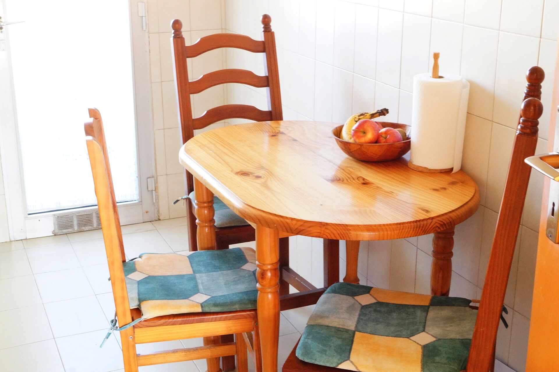 A wooden dining table with a bowl of fruit and a roll of paper towels.