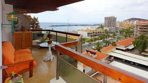 Un balcón con vista al mar, una silla de madera, una mesita y una planta en maceta.
