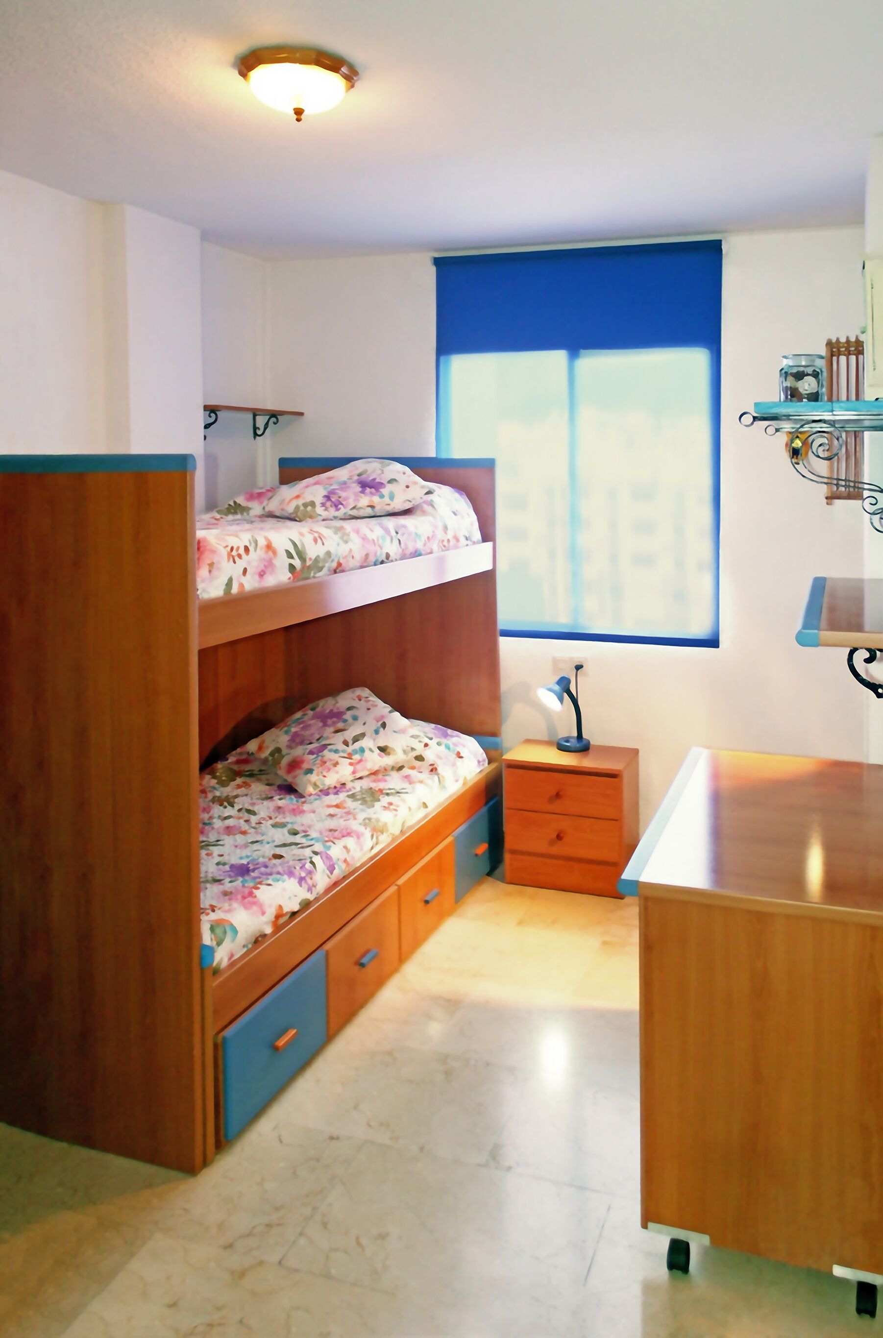A room with a bunk bed, a desk, a chair, and a window with blinds.