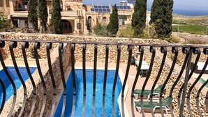 A pool with a stone border, a stone wall, and a view of buildings with solar panels. - Il- Liedna Farmhouse with private pool and beautiful views..................... (Gharb)