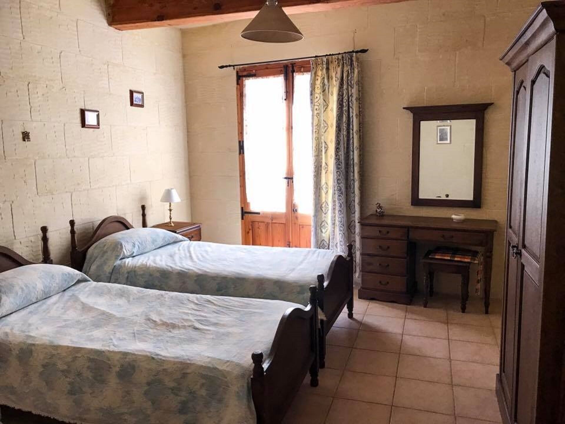 Un dormitorio con dos camas, un aparador de madera, un espejo y una ventana con cortinas.