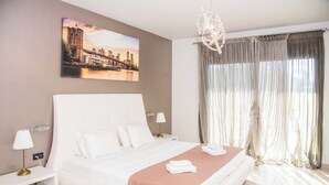 Una habitación de hotel con una cama grande, una mesita de noche, una lámpara, un cuadro de un puente y cortinas translúcidas.
