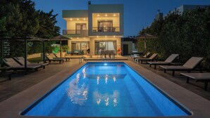 Una casa moderna de dos pisos con piscina, sillas de descanso y un área de patio.